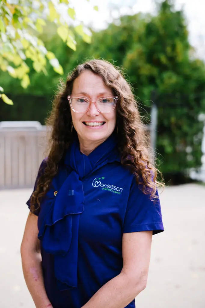 Smiling woman with curly hair in a blue uniform outdoors.