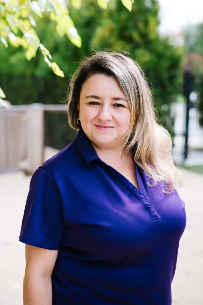A woman in a blue polo shirt smiling outdoors.