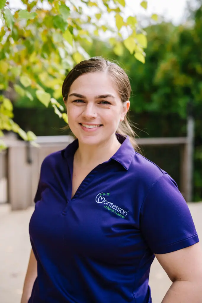 Smiling woman in a purple polo shirt outdoors.