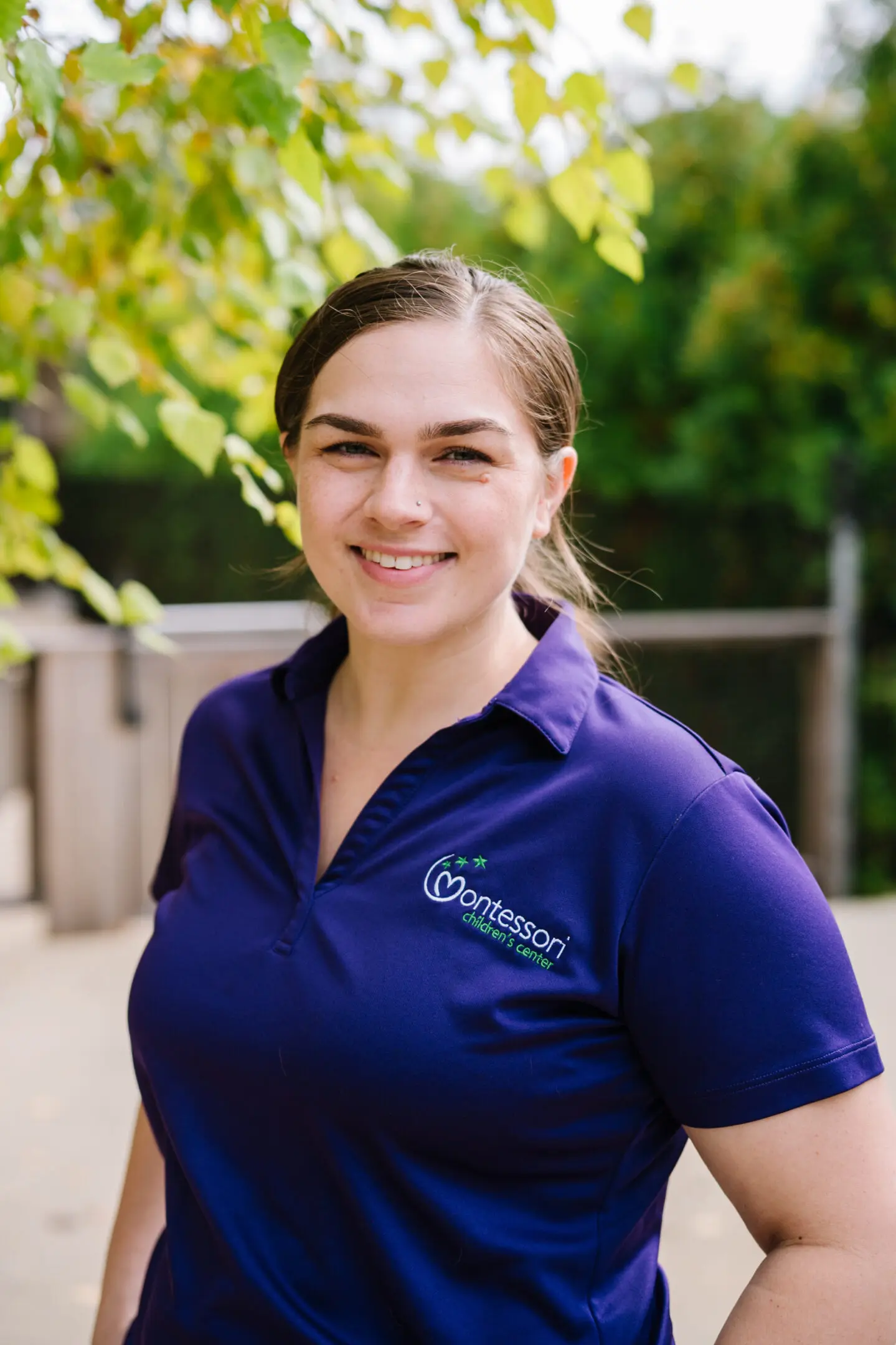 Smiling woman in a purple polo shirt outdoors.