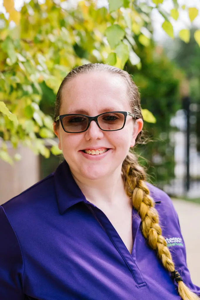 Smiling woman with glasses and a braided ponytail outdoors.