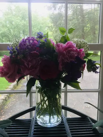 A vibrant bouquet of pink and purple flowers in a clear glass vase by a window.