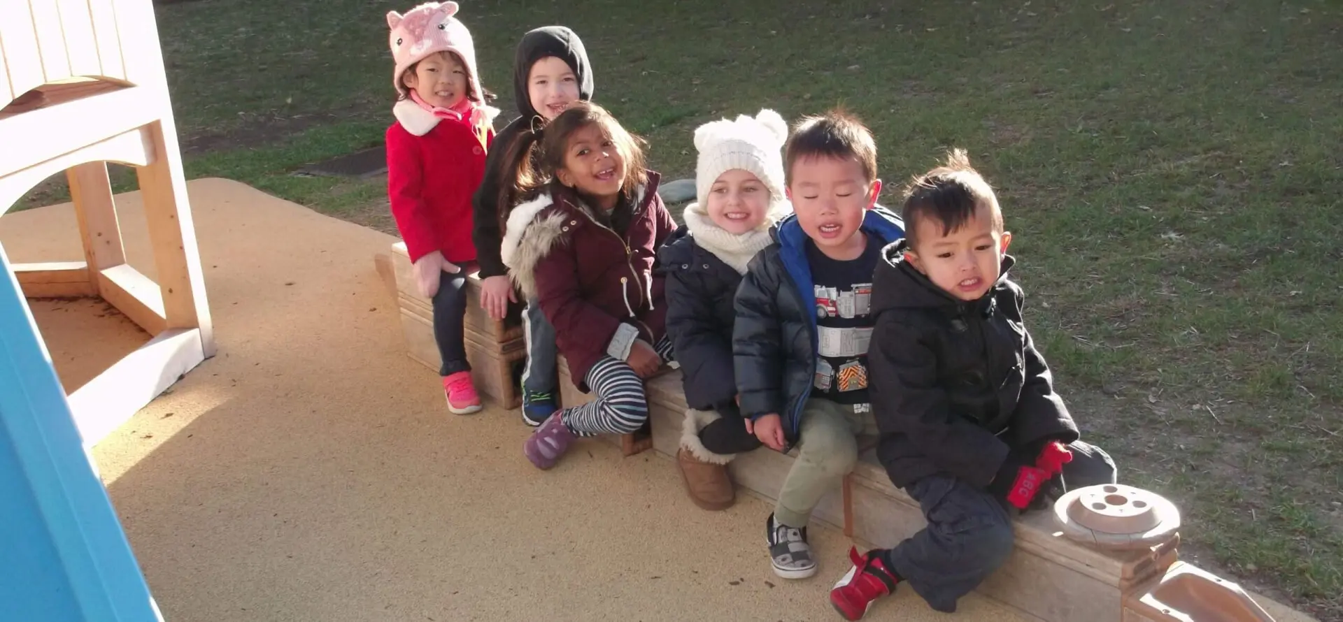 Children sitting outdoors in winter clothing.