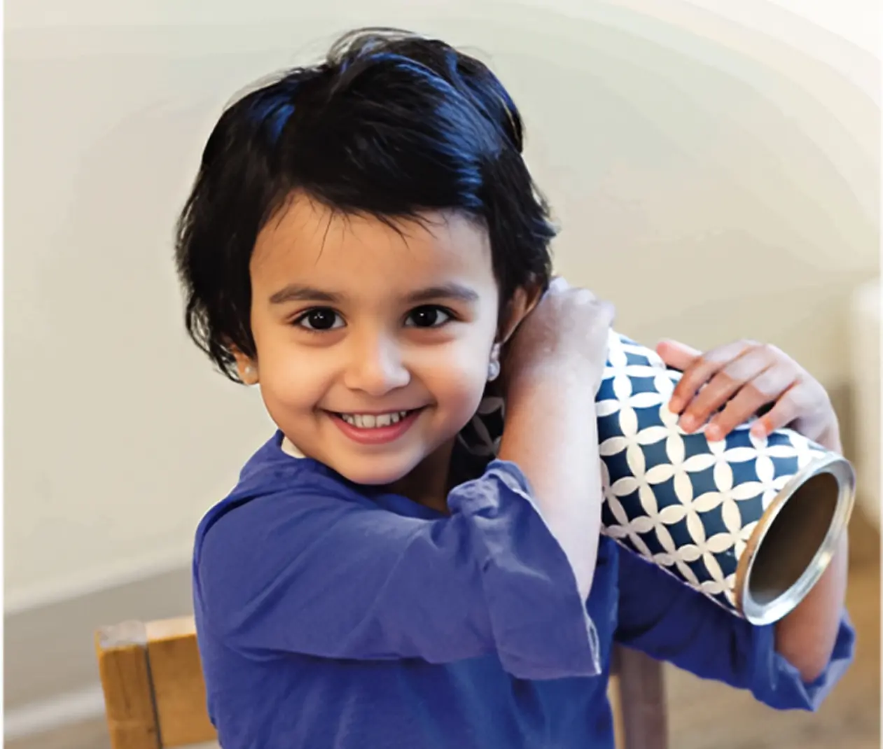 Child smiling, holding decorative blue cylinder.