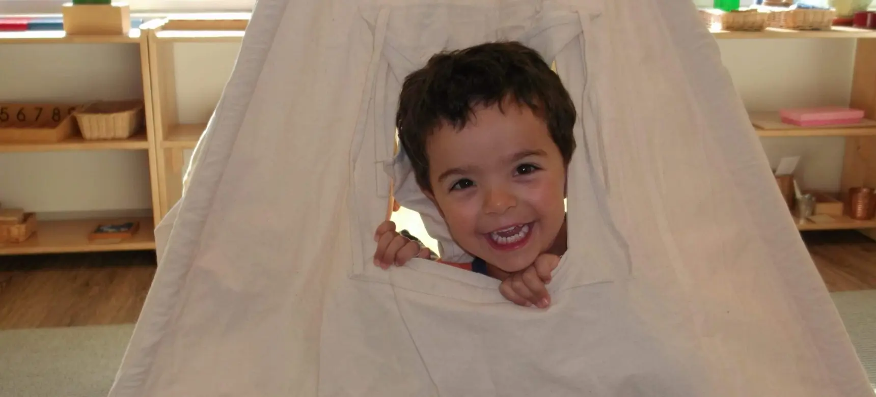 Child smiling through fabric tent opening.