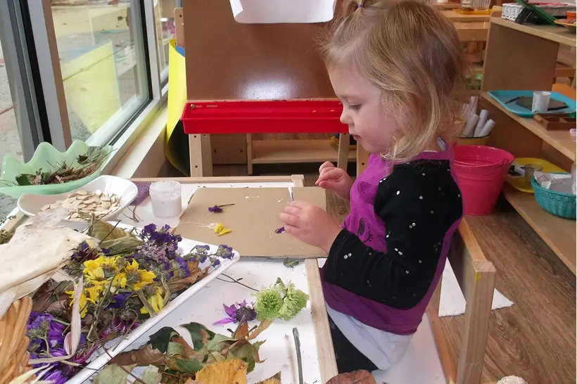 Child crafting with flowers at table.