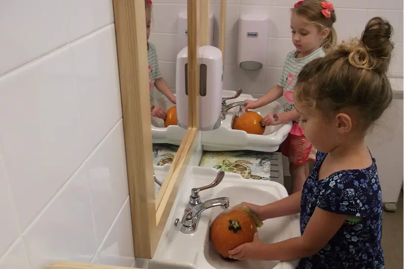 Children washing pumpkins in a bathroom sink.