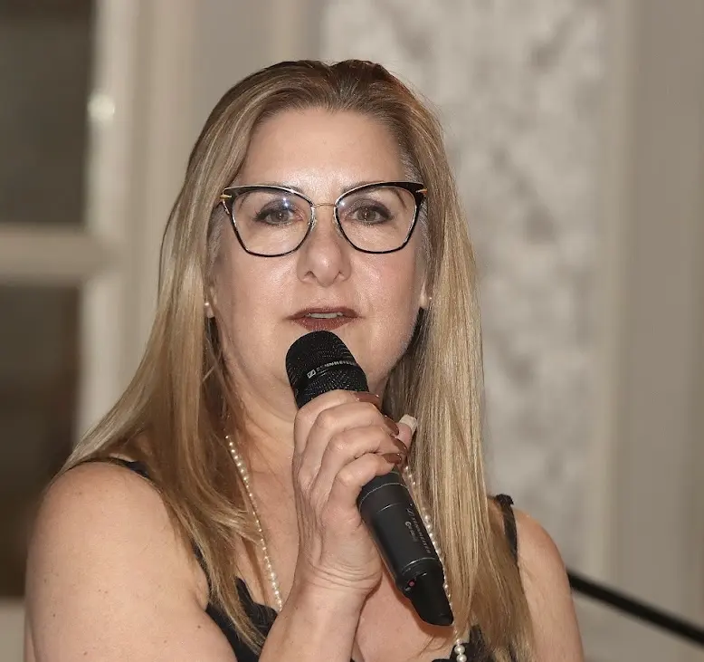 Woman speaking into a microphone at an indoor event.
