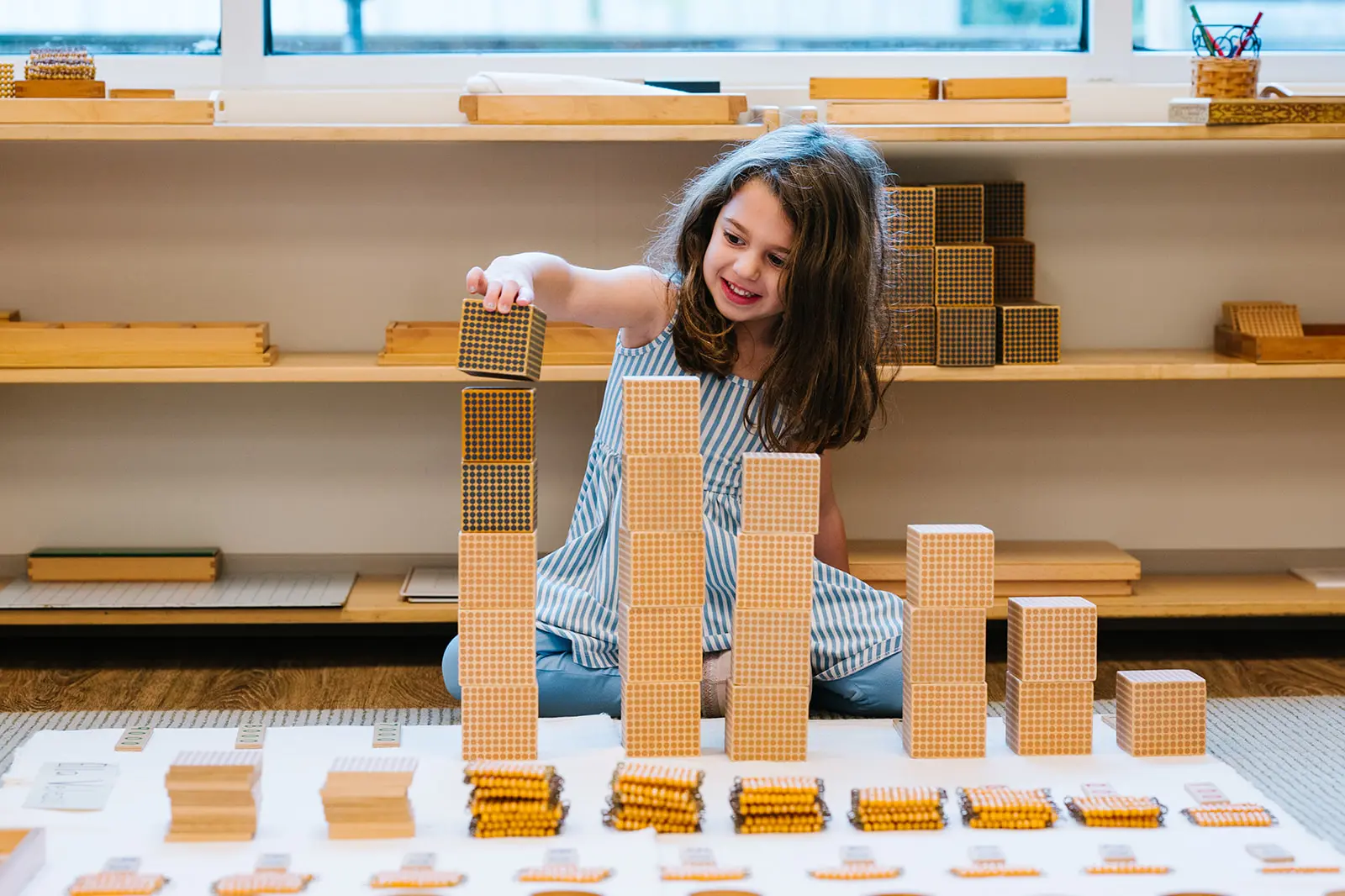 A girl stacks wooden blocks in ascending order with toy cars in front.