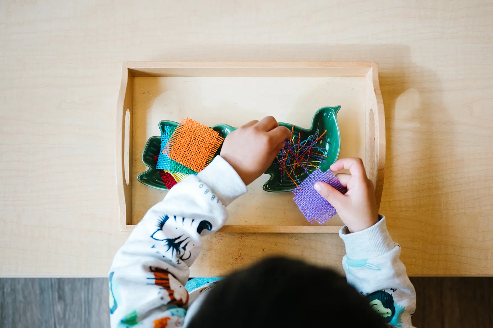 A child playing with colorful felt fish on a tray.