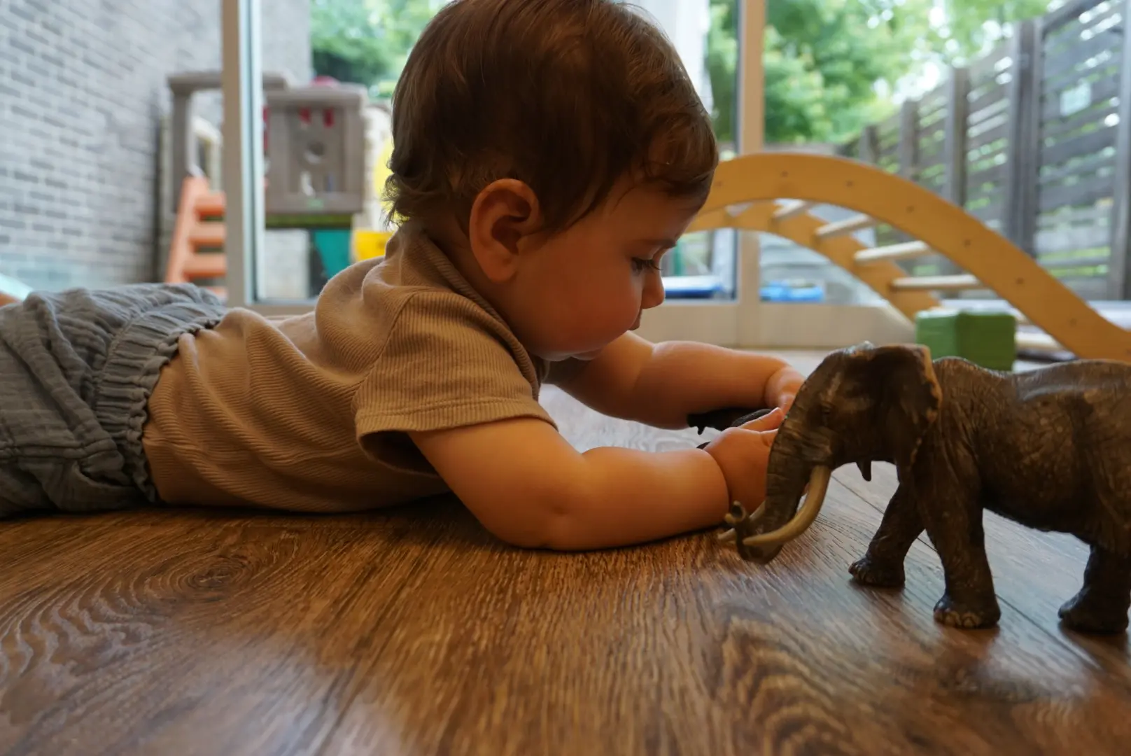 A baby playing with a small elephant figurine on a wooden table.