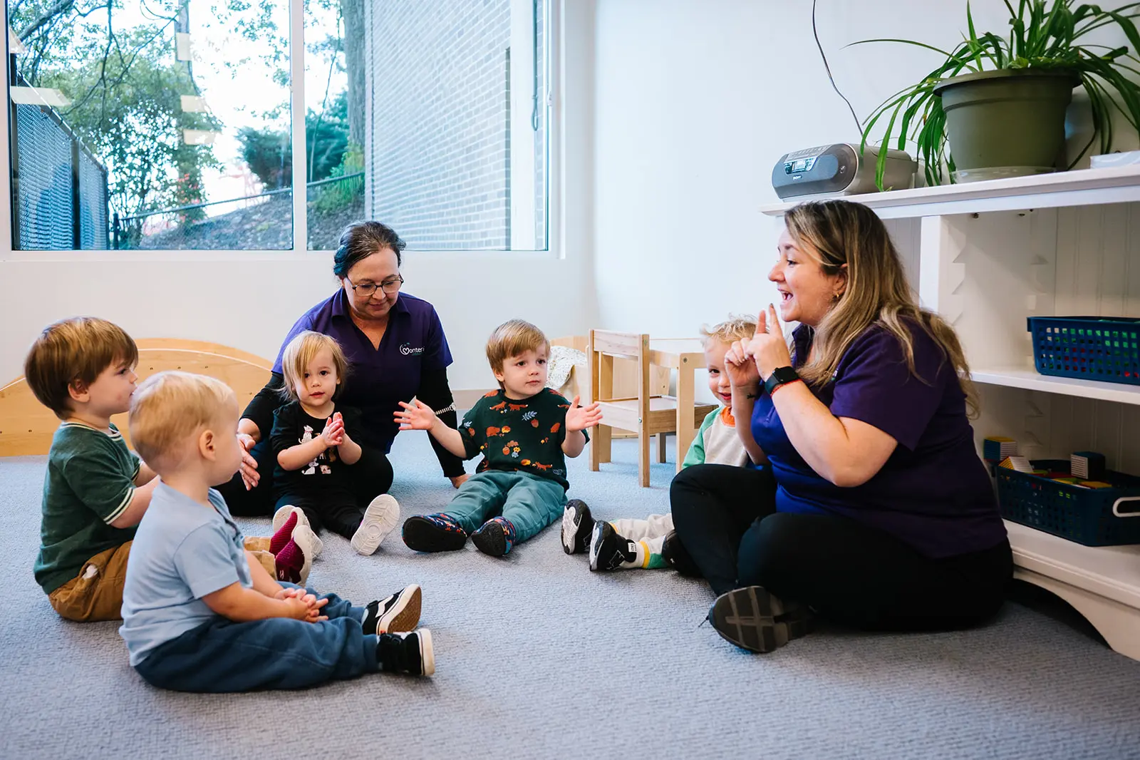 Two women engaging toddlers in a playful group activity indoors.