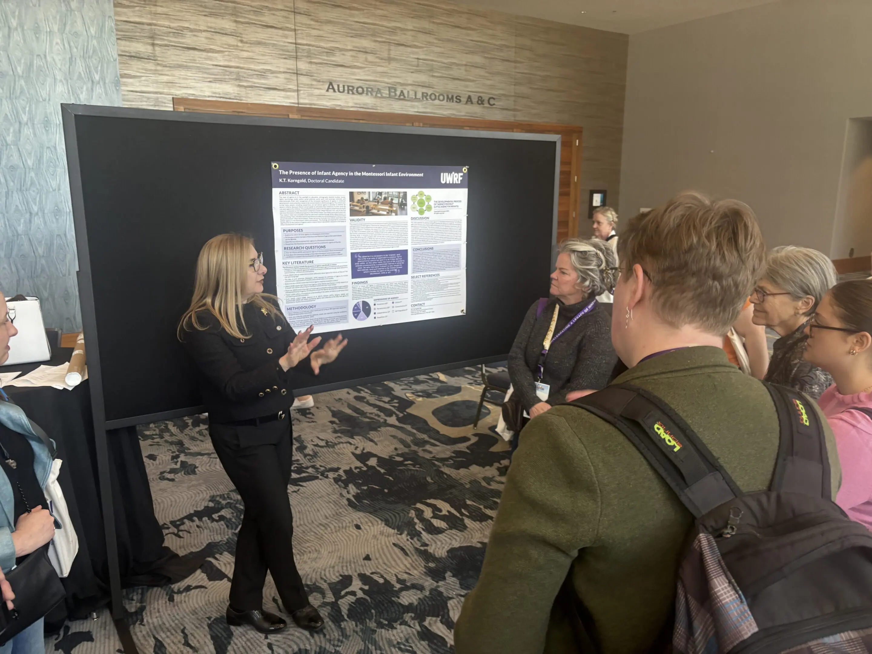 Woman presenting research poster to attendees in a conference room.