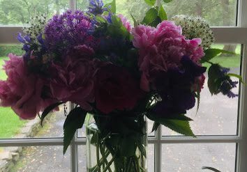 A vibrant bouquet of pink and purple flowers in a clear glass vase by a window.