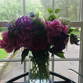 A vibrant bouquet of pink and purple flowers in a clear glass vase by a window.